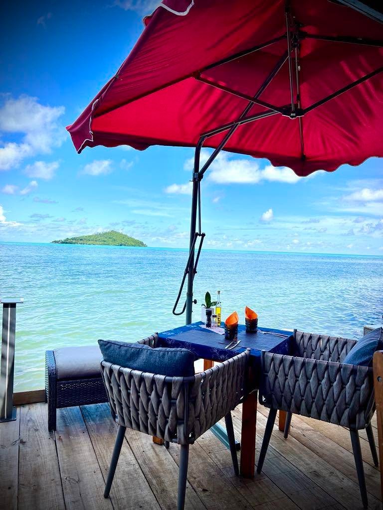 Table dressée face au lagon turquoise sous le parasol rouge du Beach Club Wallis